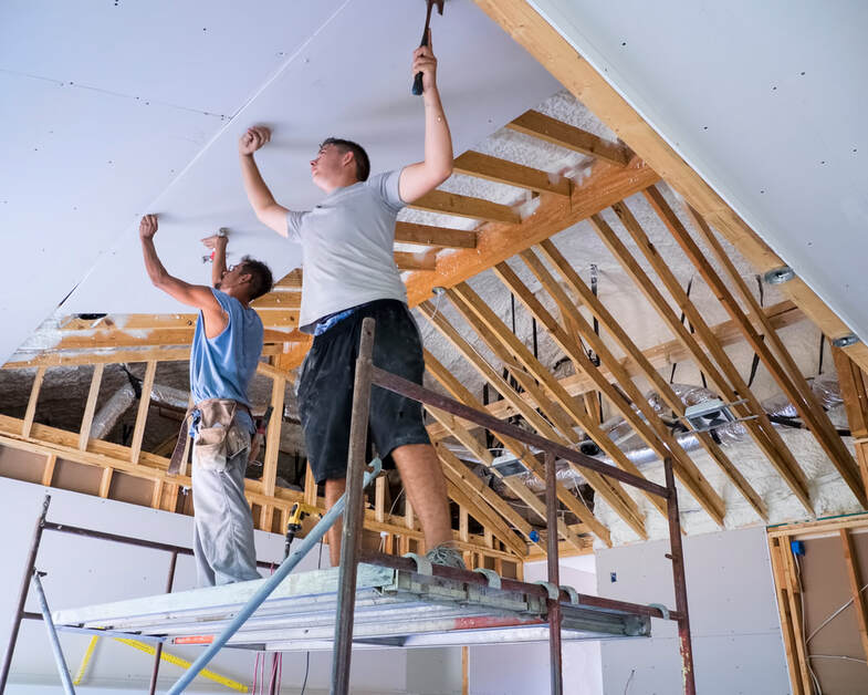 Two guys installing drywall onto a ceiling in Blackfalds, Alberta. It usually takes two guys to do this task.